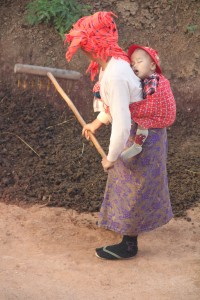 Devant sa maison, une femme travaille la terre avec son bébé sur le dos (© Aurélie Bacheley).